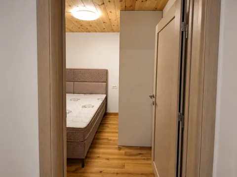 Pogled iz hodnika na spavaću sobu sa krevetom i drvenim plafonom. - image 16