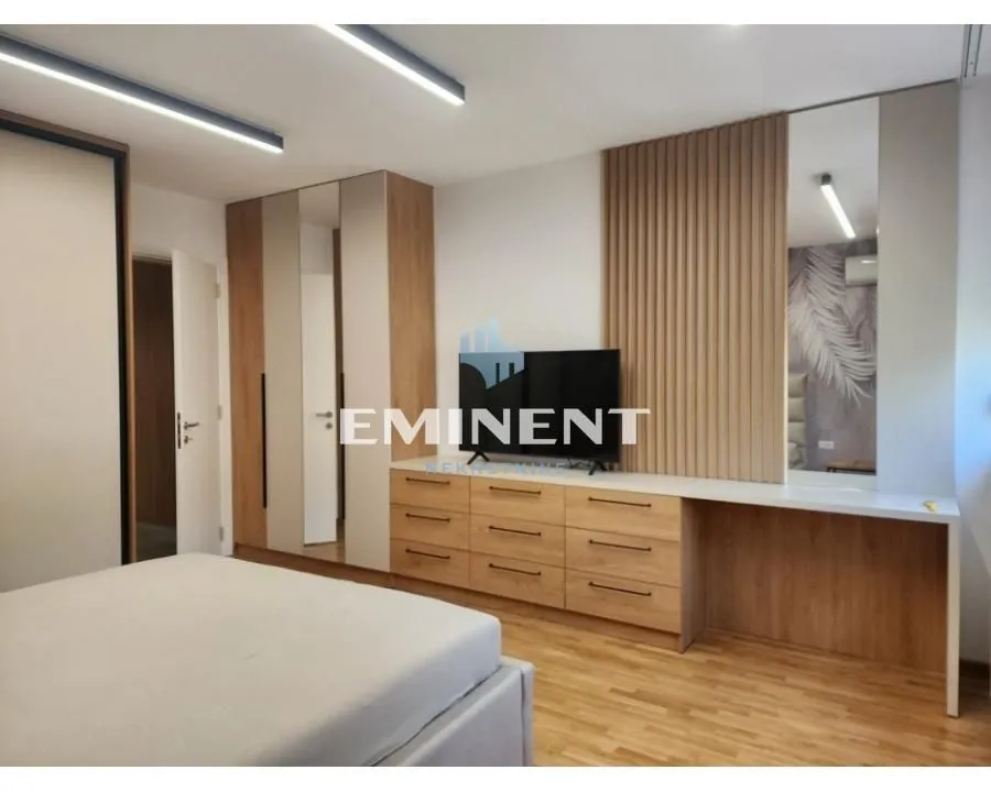 Furnished bedroom with a double bed, built-in wardrobes, and a chest of drawers with a TV.