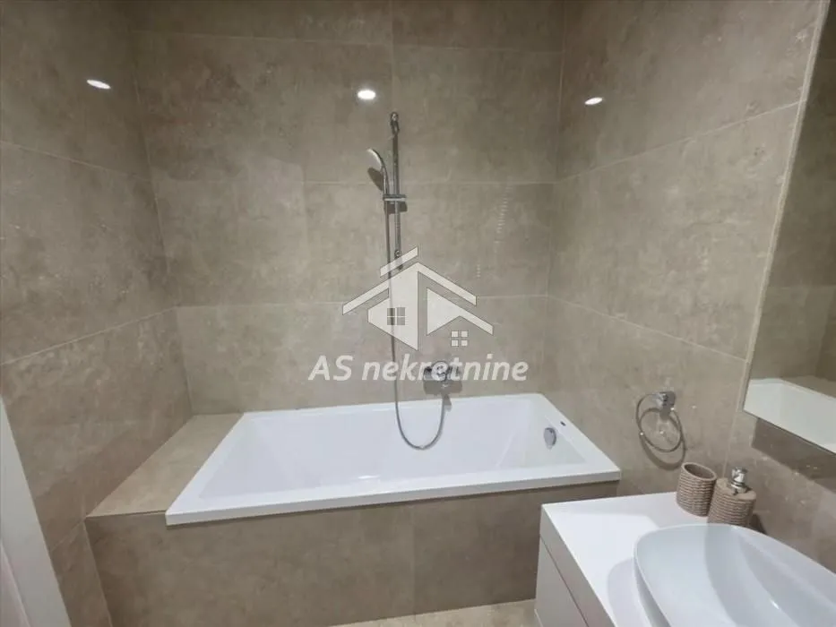Bathroom equipped with a bathtub, washbasin, and beige ceramic tiles.