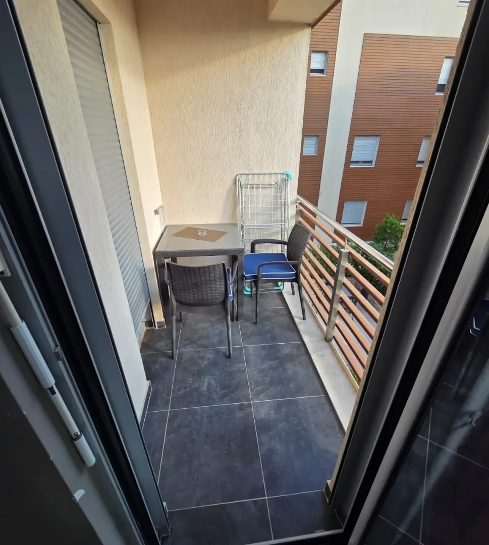 Small furnished balcony with a table, chairs, and a drying rack.