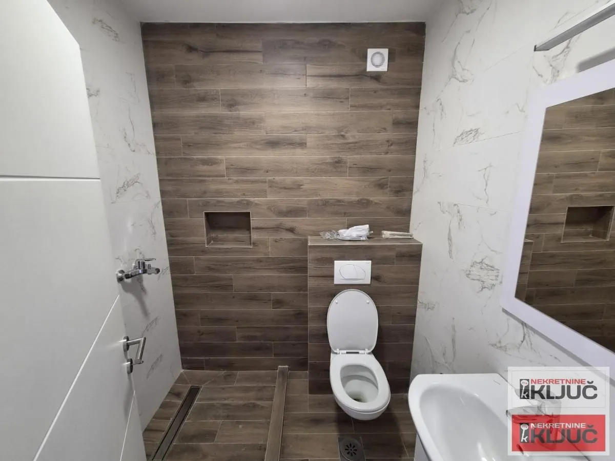 Manje kupatilo sa WC šoljom, umivaonikom i tuš kabinom.