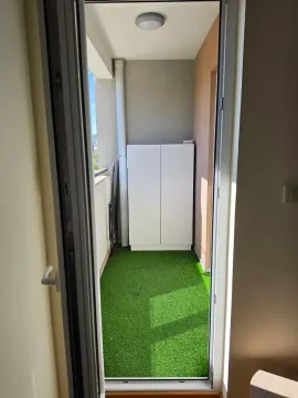 Pogled kroz vrata na uređeni balkon sa vještačkom travom i ormarićem. - image 11