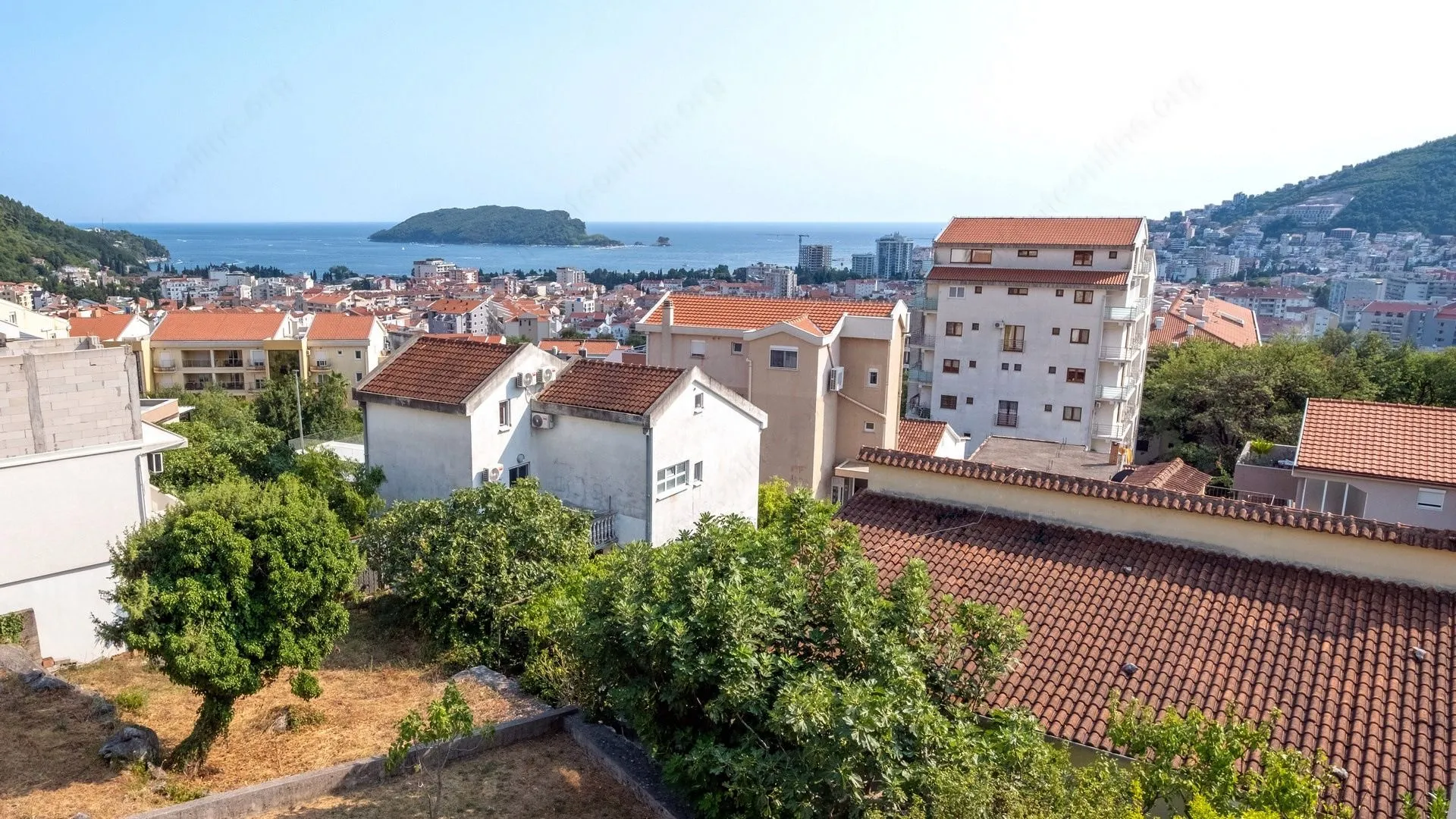 Pogled sa nekretnine na grad, krovove i more sa ostrvom u daljini.