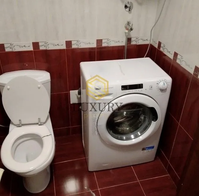 Manje kupatilo sa toaletom i veš mašinom obloženo tamnim pločicama.