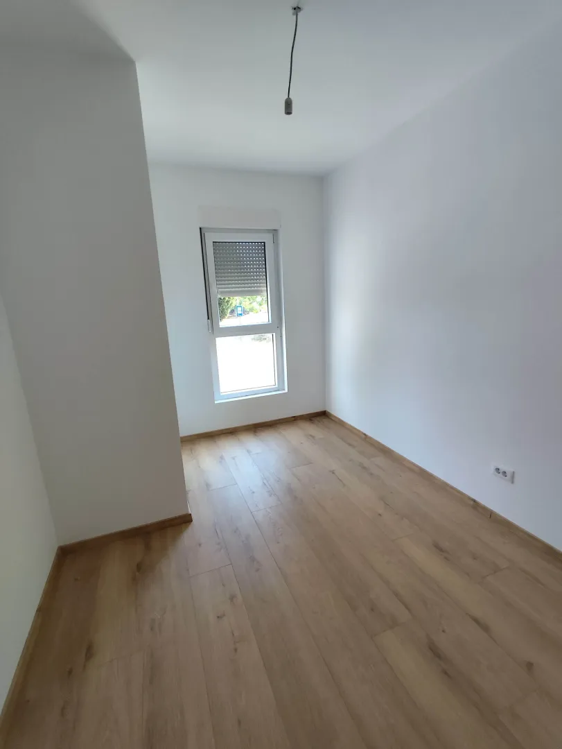 Empty bright room with wooden flooring and a single window.