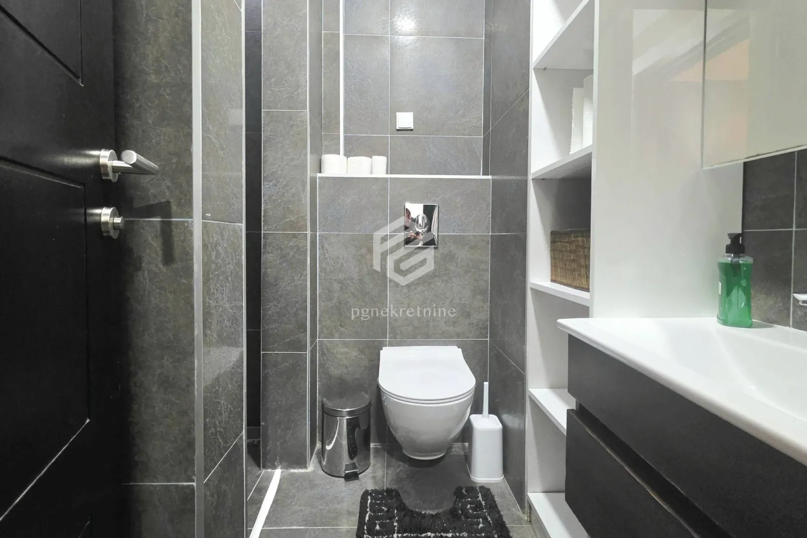 Modernly equipped bathroom with grey tiles and built-in fixtures.