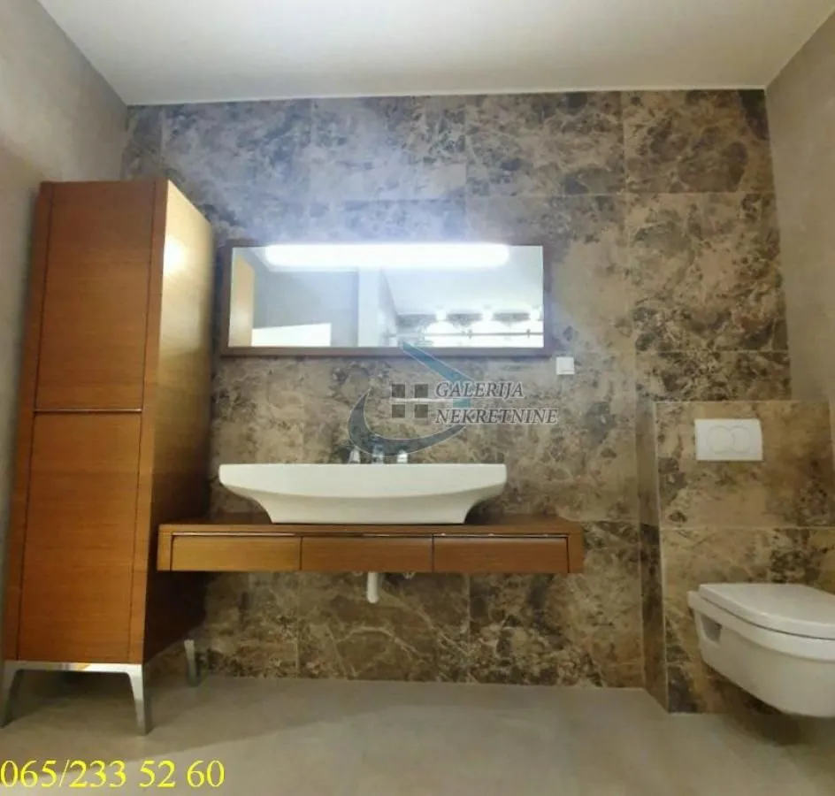 Moderno kupatilo sa umivaonikom, ogledalom, ormarićem i WC šoljom obloženo mermernim pločicama.