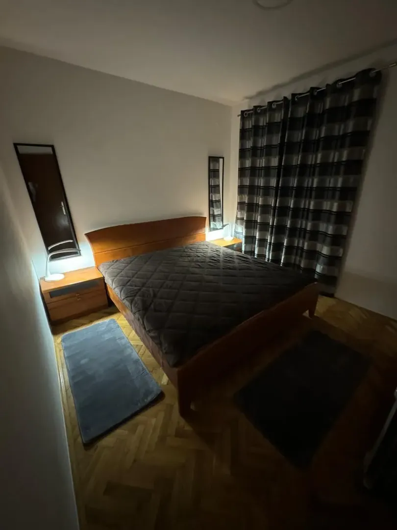 Spavaća soba sa bračnim krevetom, noćnim stočićima i prozorom sa zavjesama.