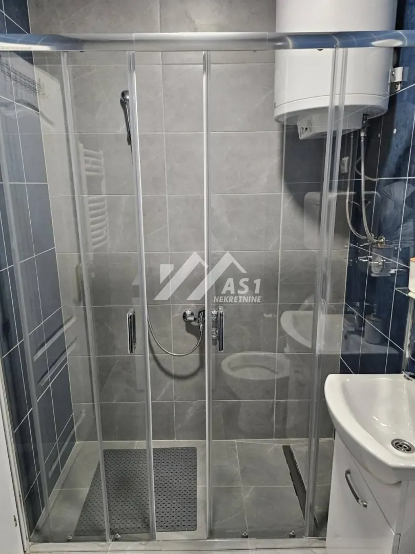 Manje kupatilo sa tuš kabinom, umivaonikom i bojlerom.