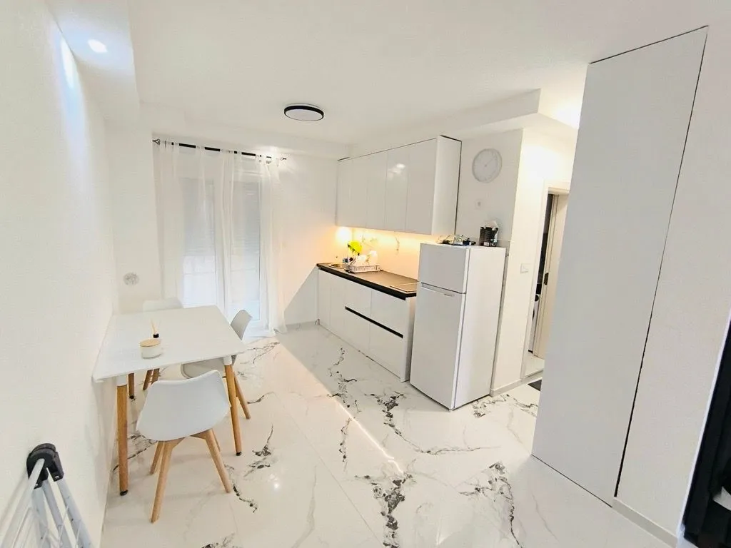Modern white kitchen with a dining table and marble floor.