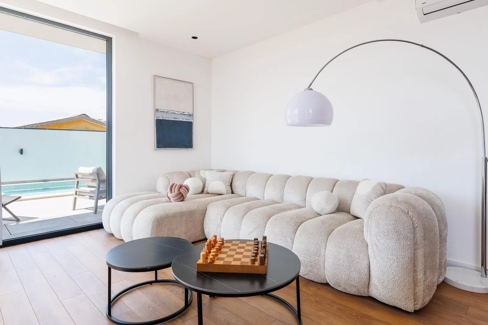 Living room with a comfortable sectional sofa, coffee table with a chess set, and access to a terrace with a pool.