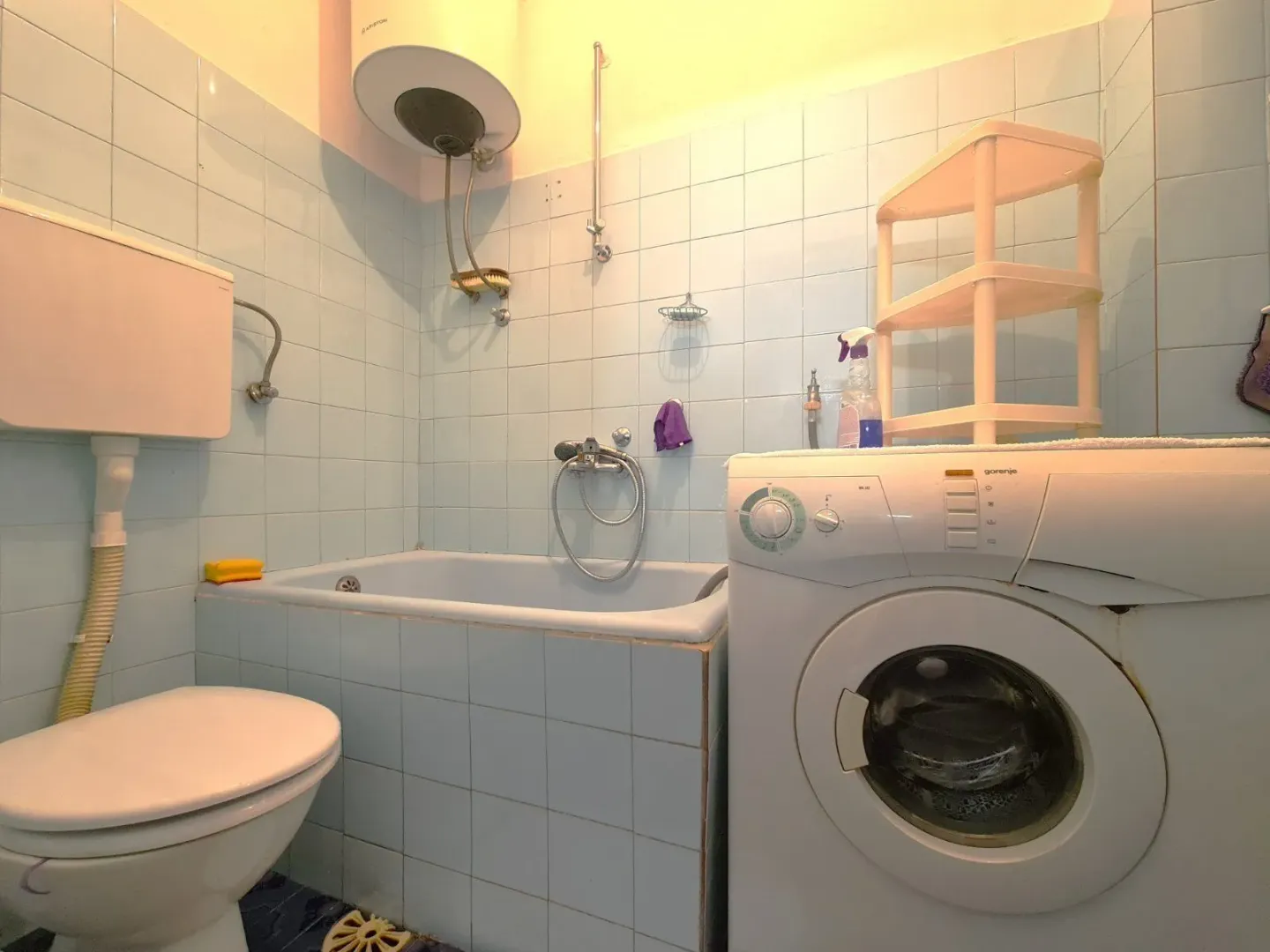 A bathroom featuring blue tiles, a small bathtub, and a washing machine.
