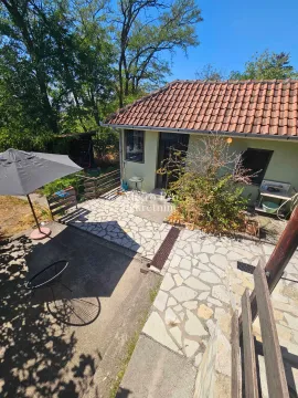Pogled na dvorište i prizemnu kuću sa popločanom terasom i suncobranom. - image 2