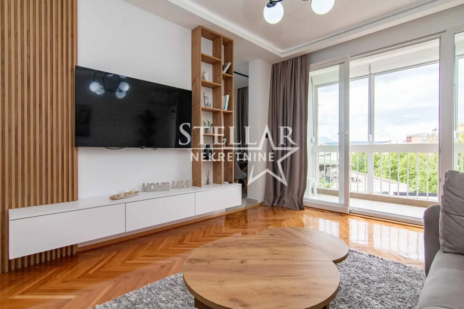 Living room with a TV unit, wooden wall panels, and access to the balcony.