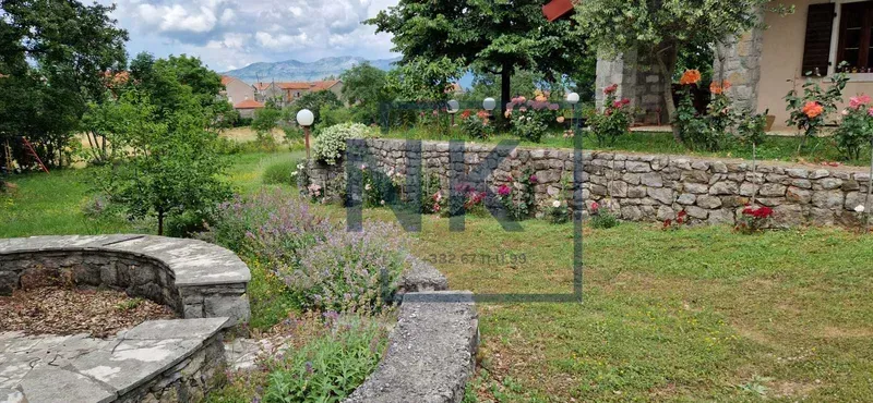 Uređeno dvorište sa kamenim zidovima i zelenilom.