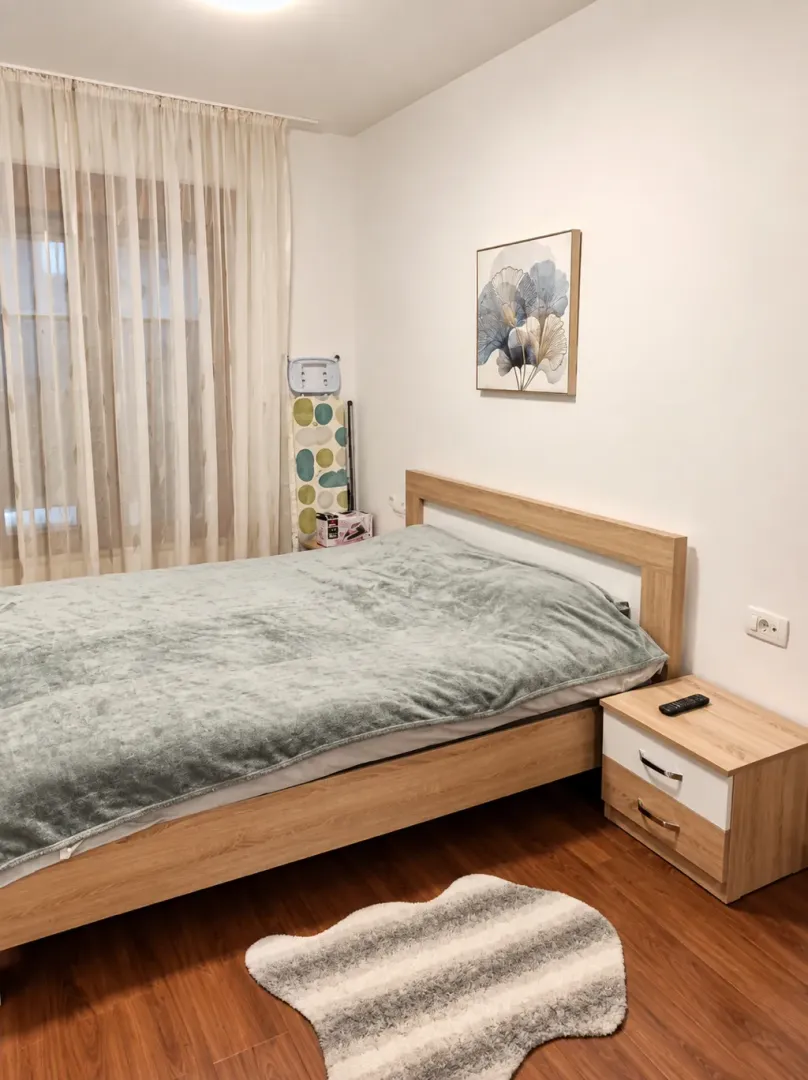 Spavaća soba sa bračnim krevetom, noćnim stočićem i prozorom sa zavjesama.