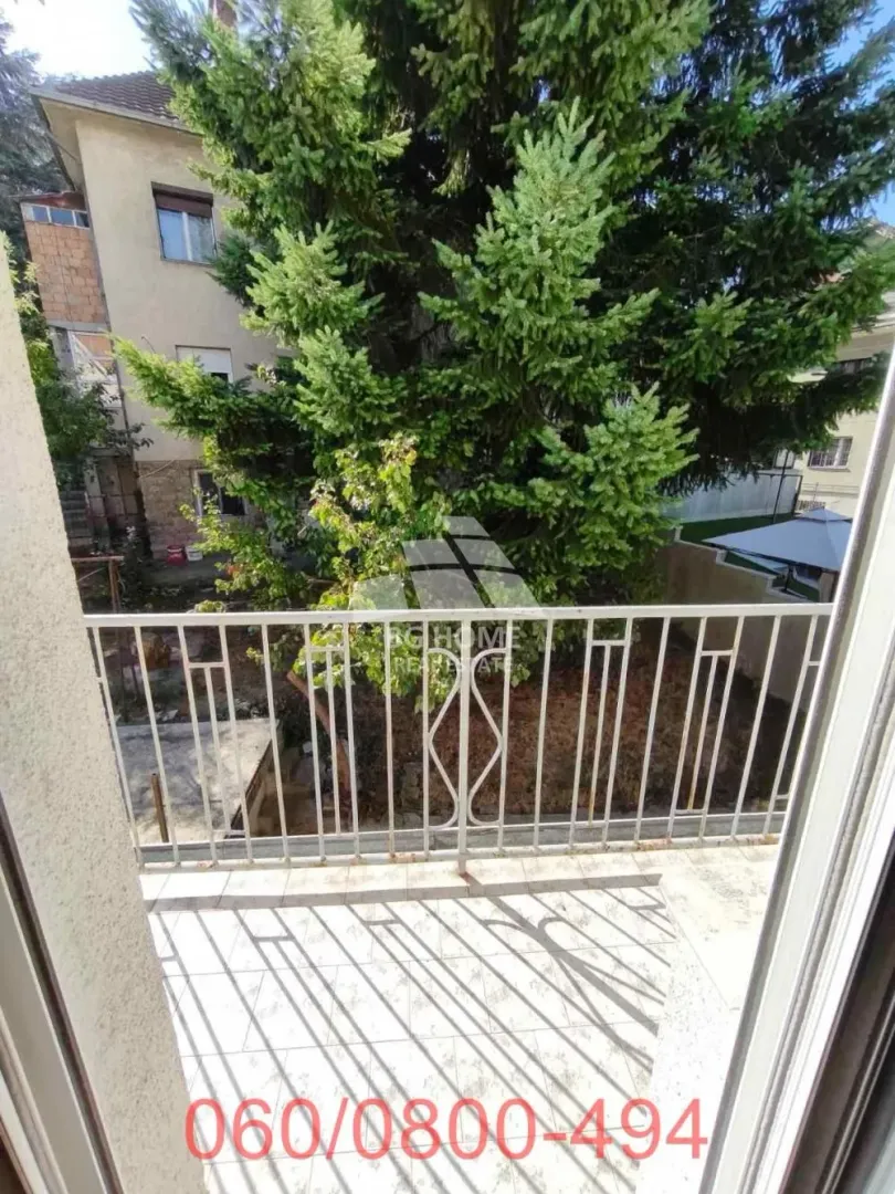 Balkon sa metalnom ogradom i pogledom na dvorište puno zelenila.