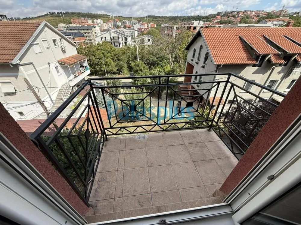 Manji popločani balkon sa crnom metalnom ogradom i pogledom na naselje.