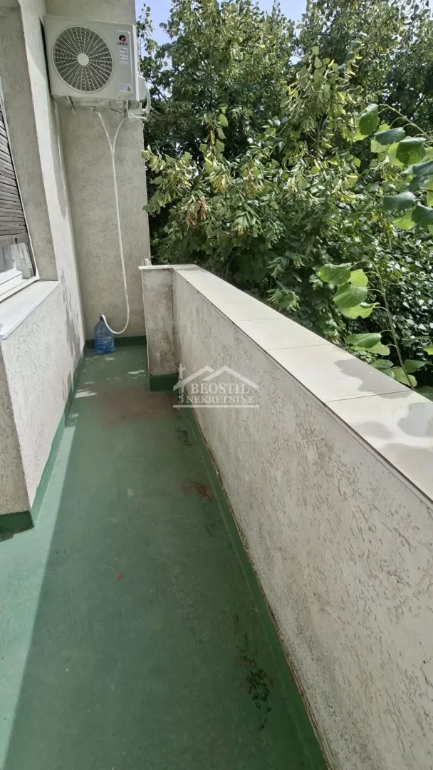 Manji balkon sa klima uređajem i pogledom na zelenilo.
