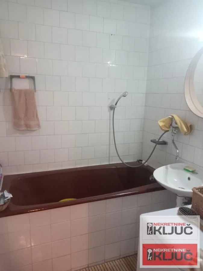 Kupatilo sa kadom, umivaonikom i belim zidnim pločicama.