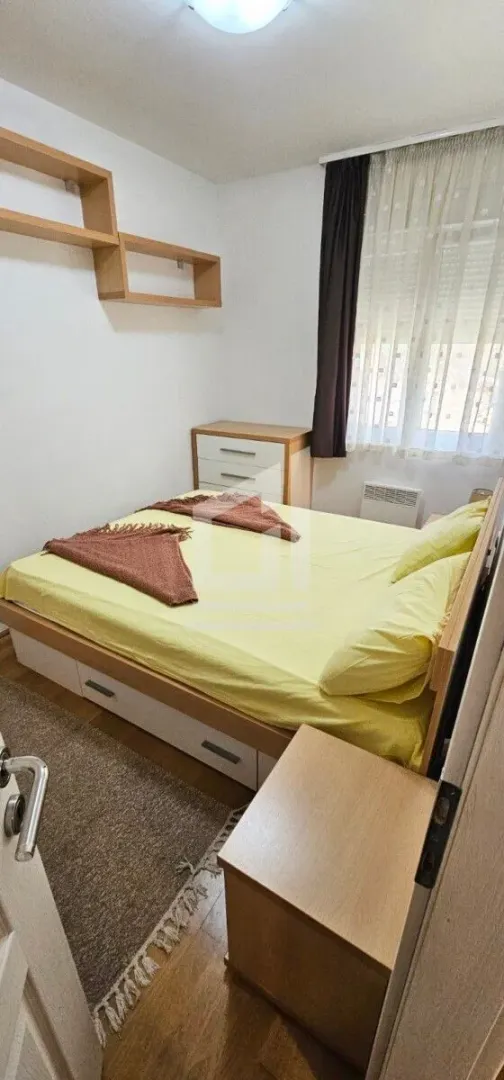 Manja spavaća soba sa bračnim krevetom, komodom i zidnim policama.