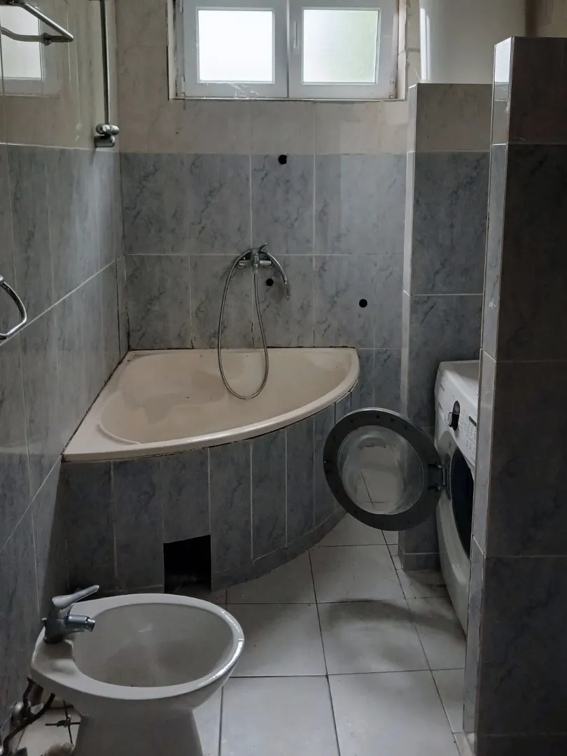 Bathroom with tiles, corner bathtub, bidet and washing machine.