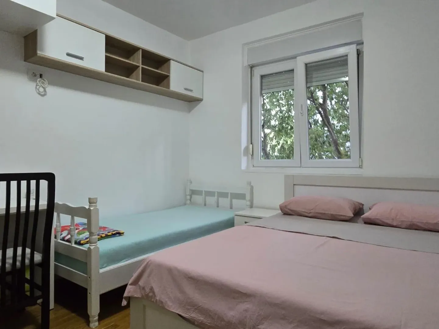Bright and tidy bedroom with a double bed, single bed, and wall-mounted shelving units.