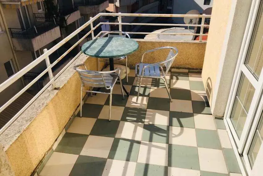 Manji namješteni balkon sa stolom i stolicama i popločanim podom.