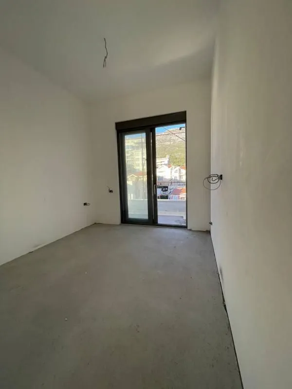 Prazna prostorija u izgradnji sa balkonskim vratima i pogledom na okolne zgrade.