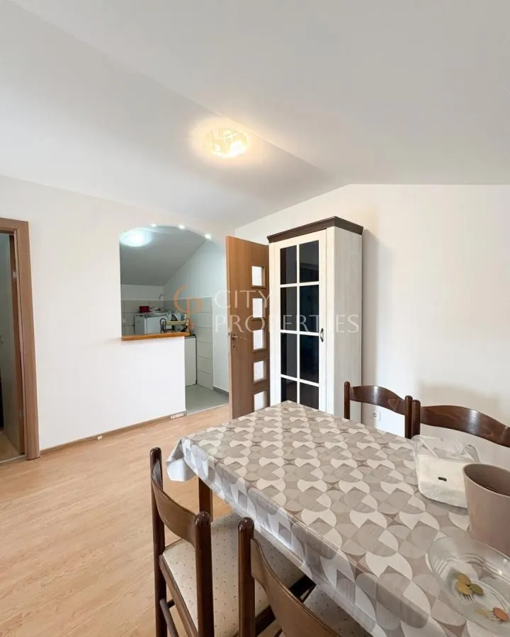 Dining area with a wooden table and chairs, looking into the kitchen through an opening.