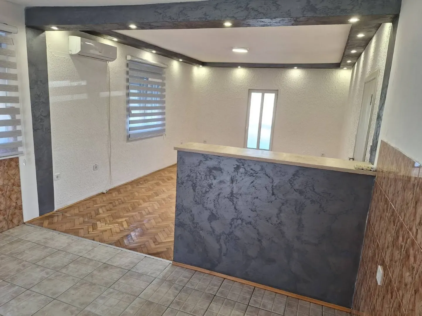 An empty, well-lit room featuring a decorative bar counter and parquet flooring.