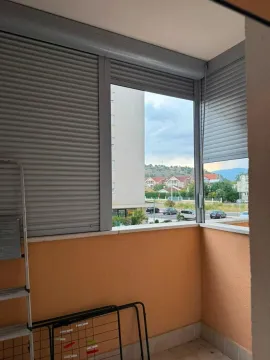 Natkriveni balkon sa roletnama i pogledom na okolne zgrade i brda. - image 12