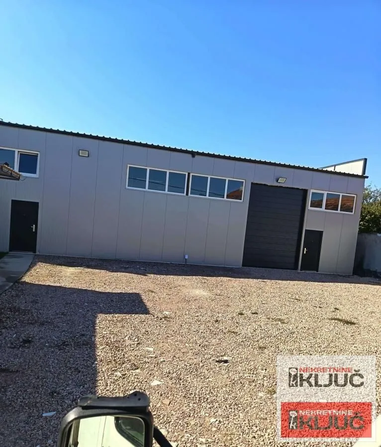 Exterior view of an industrial building with a large yard and garage doors.