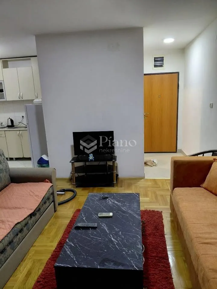 Living room with sofa, television, and a view towards the kitchen and entrance door.