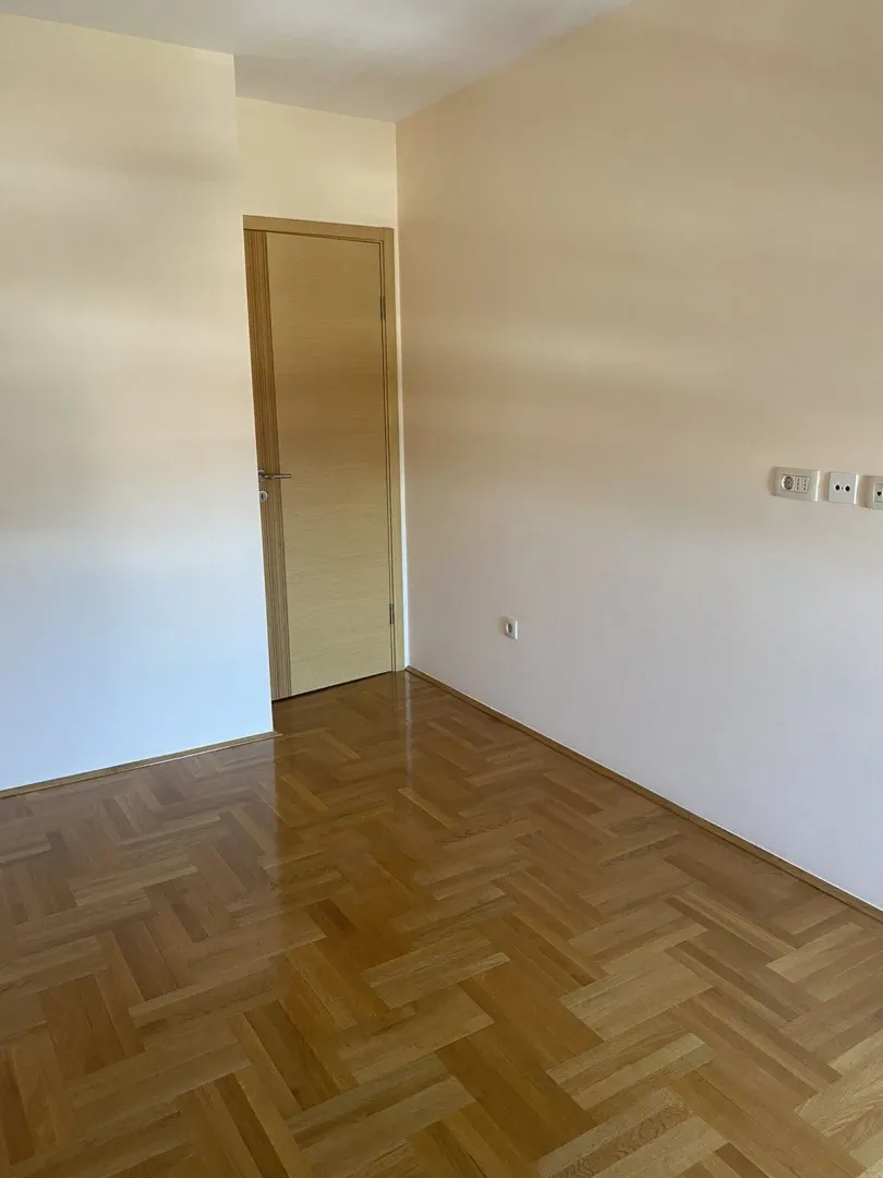 Prazna soba sa lakiranim parketom i svijetlim zidovima.