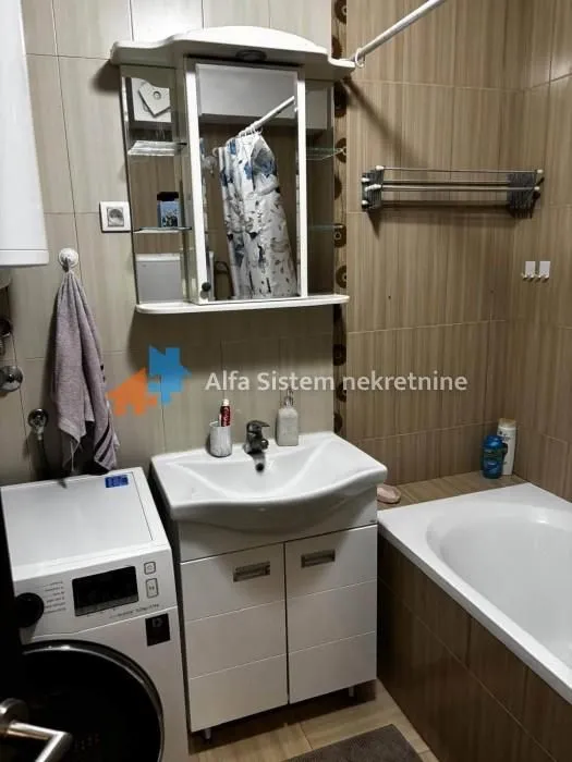 Kupatilo opremljeno umivaonikom, ormarićem, kadom i veš mašinom.