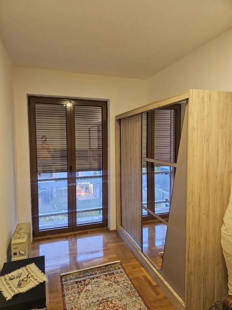 Soba sa velikim drvenim ormarom i izlazom na balkon.