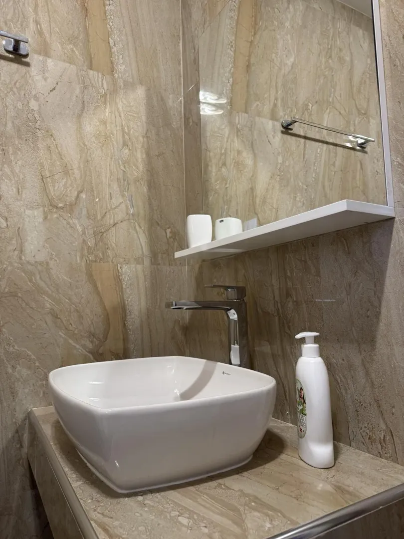 Moderni lavabo sa ogledalom u kupatilu sa mermernim pločicama.