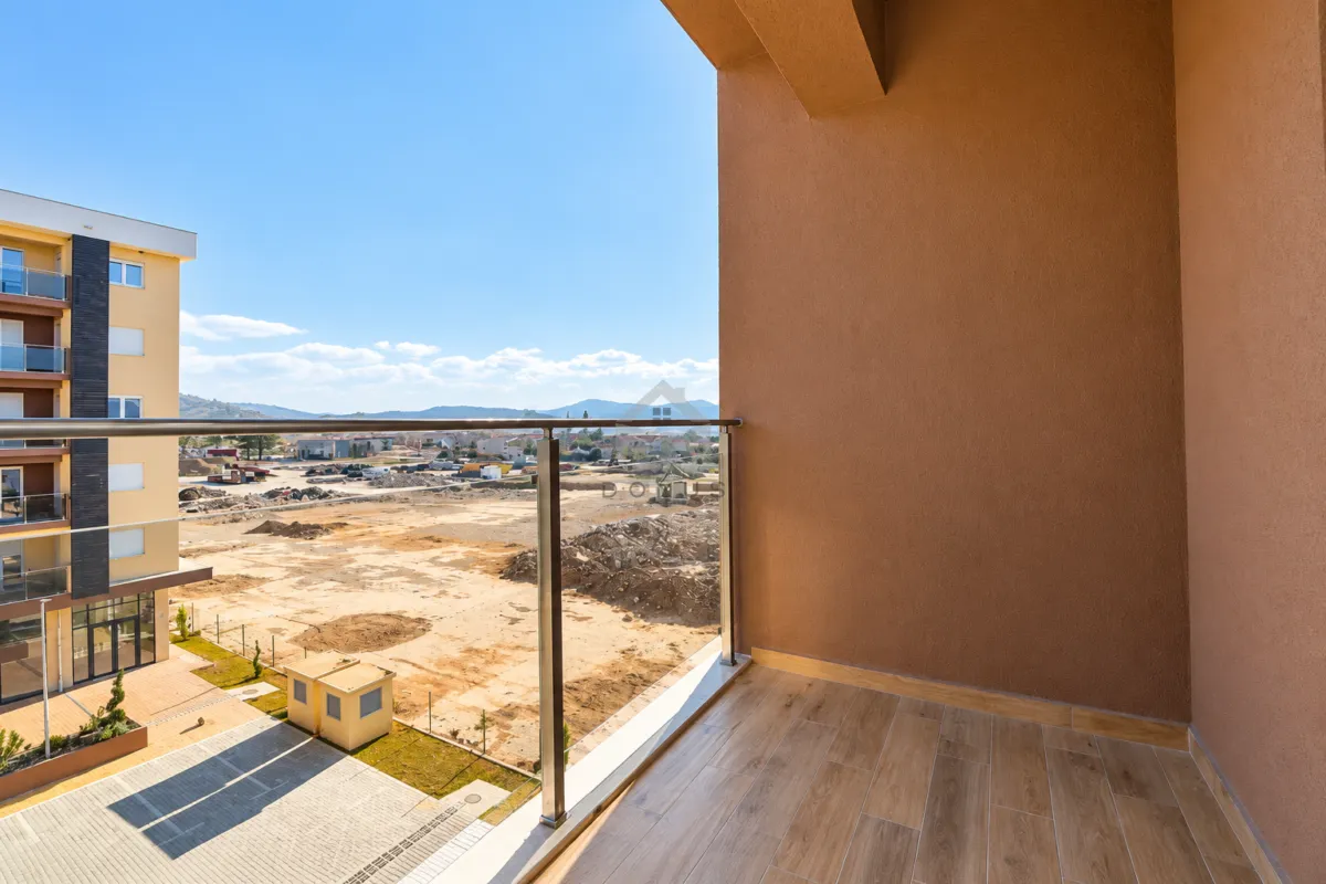 Nenamješten balkon sa staklenom ogradom i pogledom na okolinu.
