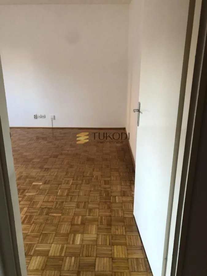 Prazna soba sa parketom i otvorenim vratima.