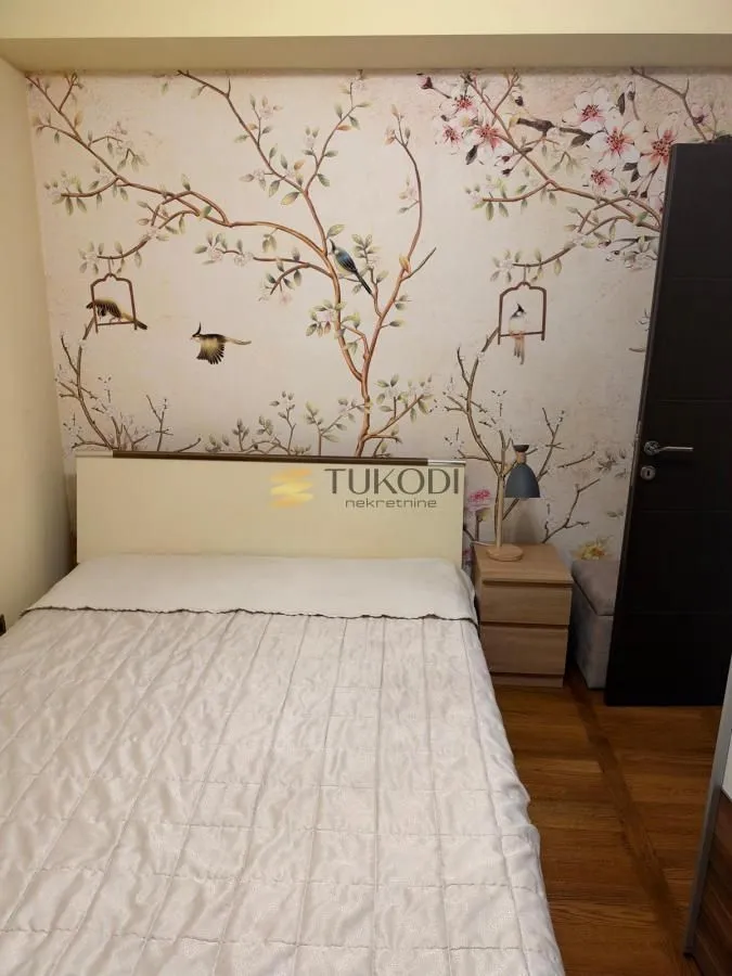Spavaća soba sa bračnim krevetom i dekorativnim tapetama na zidu.