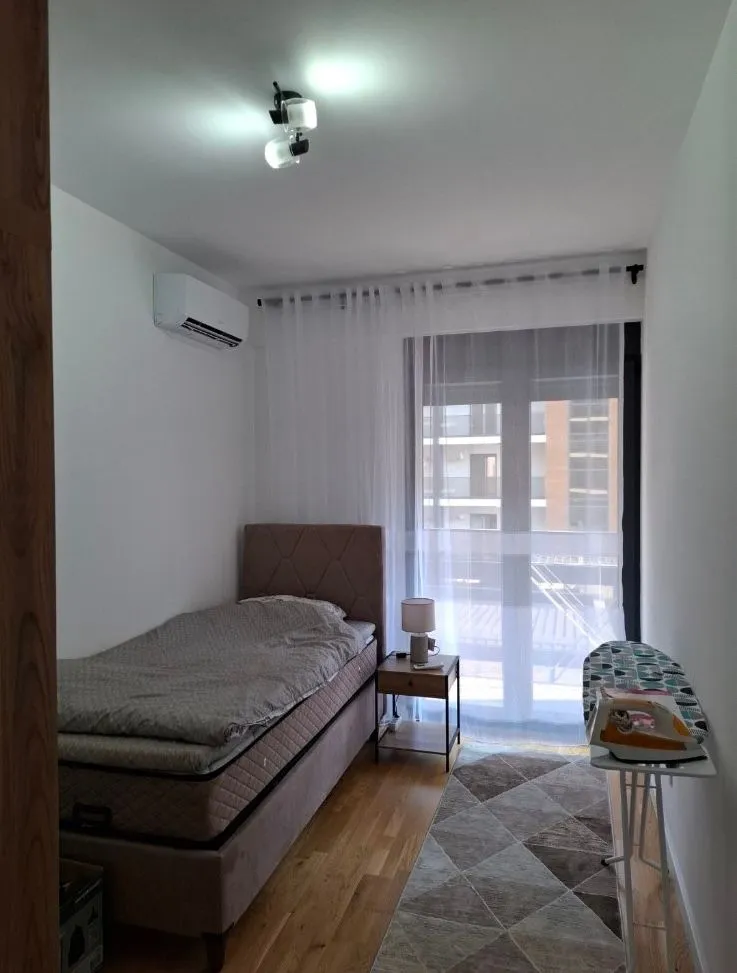 Manja spavaća soba sa krevetom, noćnim stočićem i izlazom na terasu.