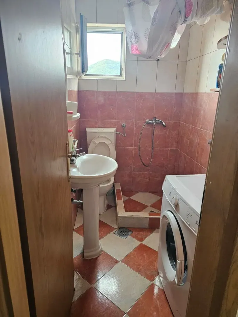 Manje kupatilo sa umivaonikom, WC šoljom, tuš kabinom i veš mašinom.