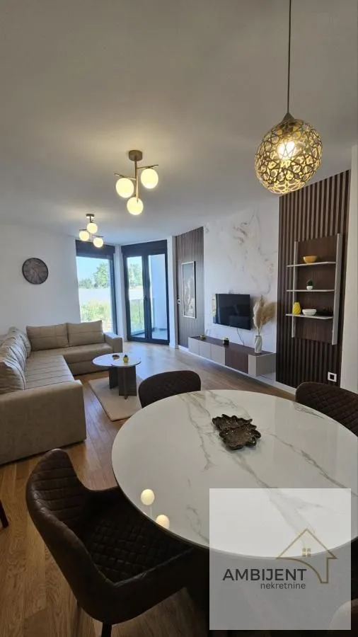 Dnevna soba sa trpezarijom, garniturom i modernim osvetljenjem.
