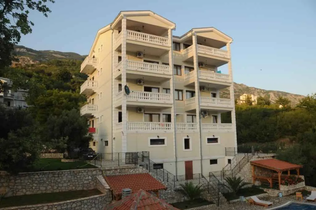 Pogled na višespratnu stambenu zgradu sa terasama i uređenim dvorištem.