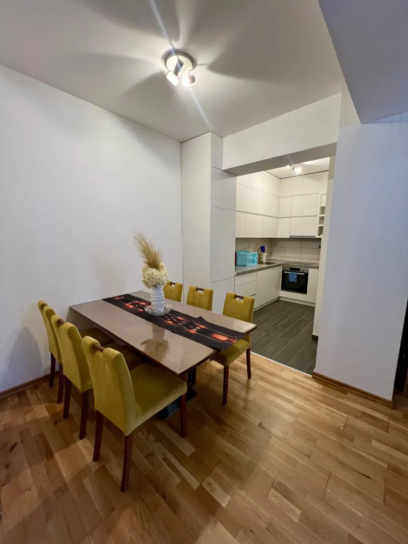 Dining area with a table and yellow chairs, with a view of the kitchen in the background.