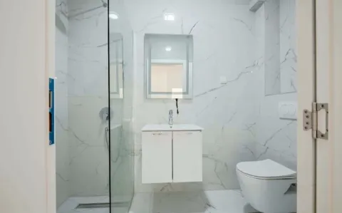 Moderne kupatilo sa bijelim mermernim pločicama, tuš kabinom i konzolnim umivaonikom. - image 6