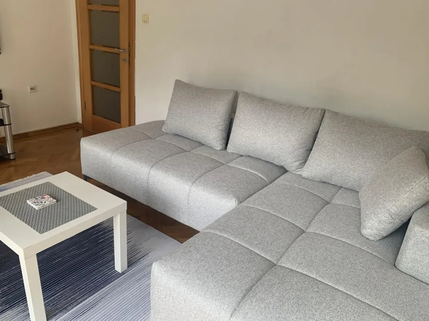 Svijetla dnevna soba sa sivom ugaonom garniturom i malim stolom.