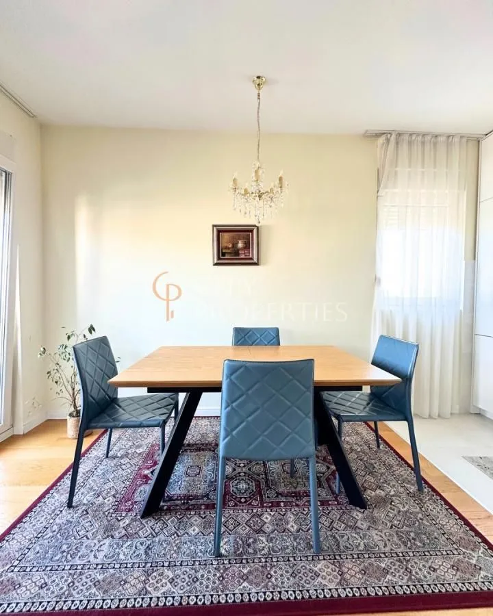 Trpezarija sa drvenim stolom i modernim stolicama na tepihu.