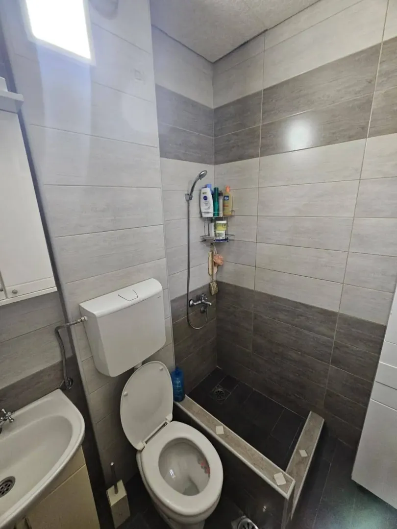 Manje kupatilo sa tuš kabinom, WC šoljom i umivaonikom obloženo keramičkim pločicama.